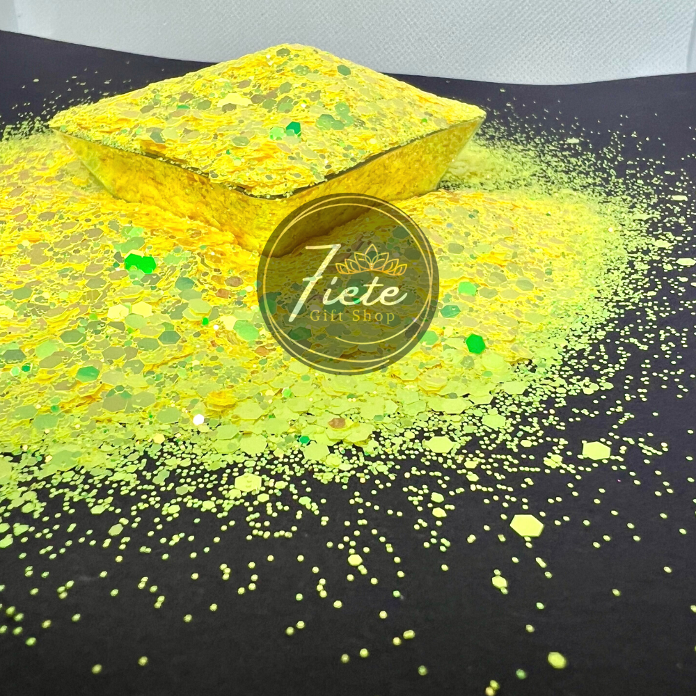 Loose glitter overflowing onto a black surface, the glitter is color changing from the dominant yellow to subtle green and golds.