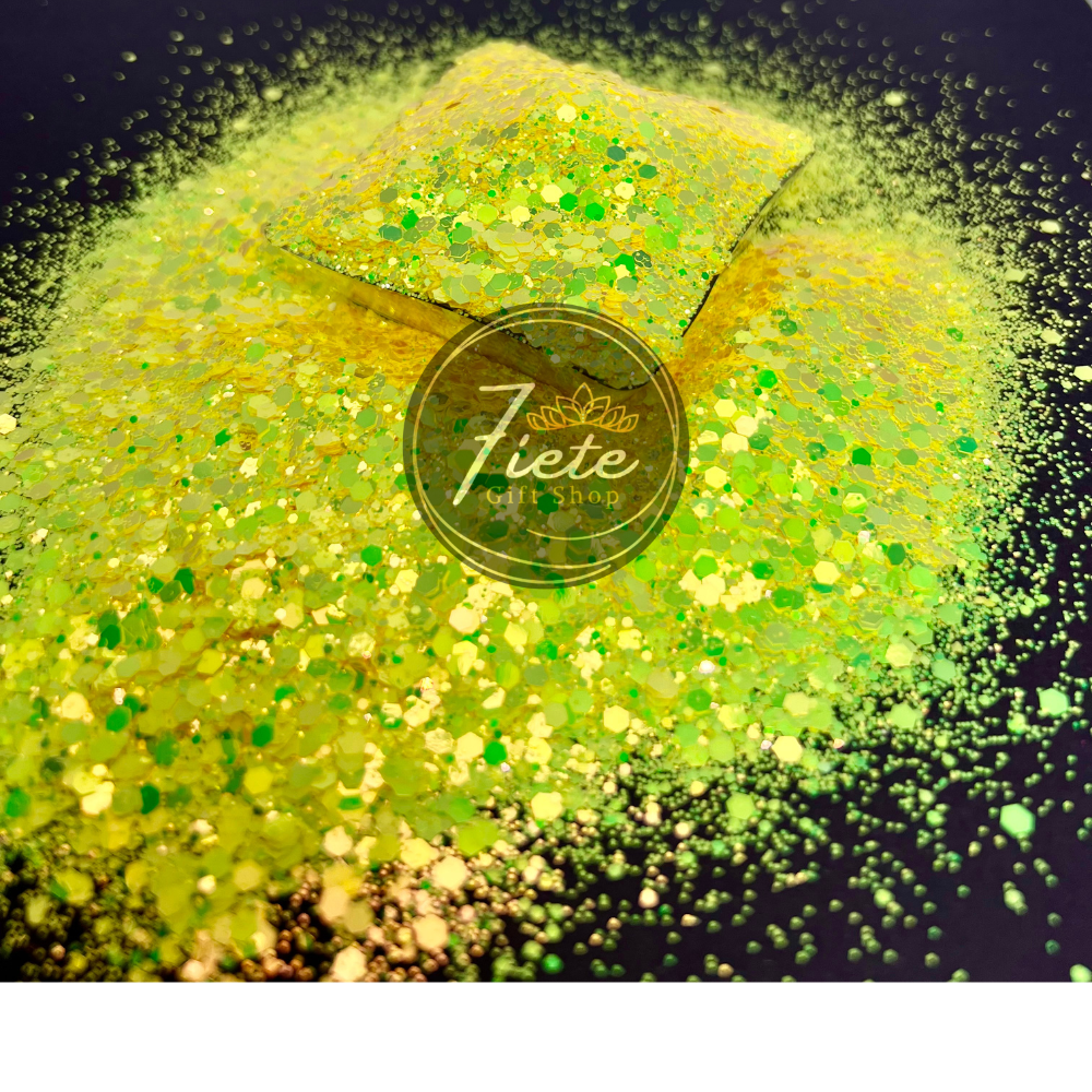 Loose glitter overflowing onto a black surface, the glitter is color changing from the dominant yellow to subtle green and golds.