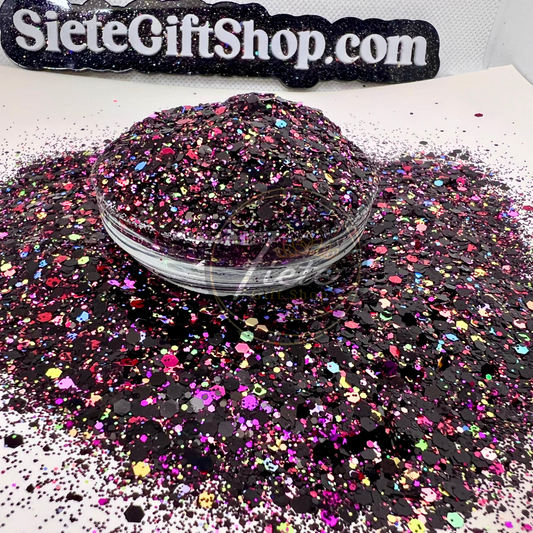 Loose glitter in a clear jar spilled over showing all the colors, black, purple, green, pink, yellow